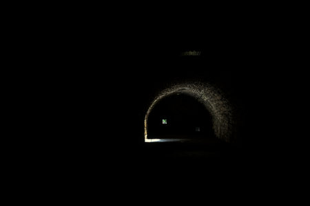 Arching passage in the dark with sunlight passing through holes and an opening in the distanceの写真素材