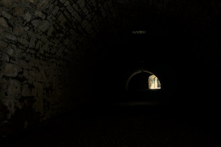 Arching passage in the dark with sunlight passing through holes and an opening in the distanceの写真素材