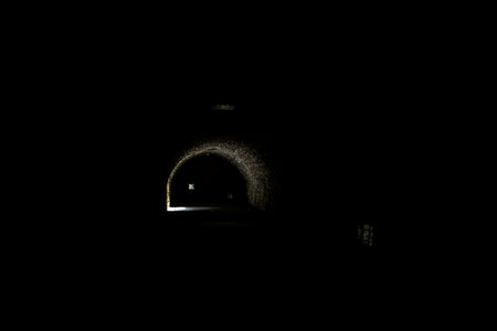 Arching passage in the dark with sunlight passing through holes and an opening in the distanceの写真素材