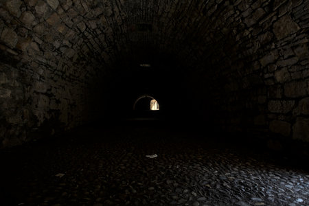 Arching passage in the dark with sunlight passing through holes and an opening in the distanceの写真素材