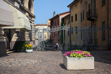Square between historic buildings with a flower pot and an iron fence on a sunny day in an Italian townの写真素材