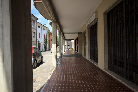 Modern porch under a building with shops closed by metallic shutters by the edge of a street on a sunny dayの写真素材