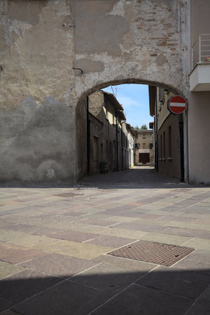 Alley in the shade with an abandoned shop at the end of it seen from an arch at the beginning of the street on a sunny day in an Italian townの写真素材