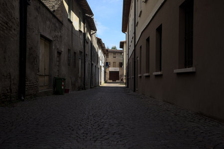 Alley in the shade with an abandoned shop at the end of it seen from an arch at the beginning of the street on a sunny day in an Italian townの写真素材