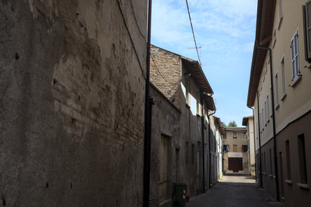 Alley in the shade with an abandoned shop at the end of it seen from an arch at the beginning of the street on a sunny day in an Italian townの写真素材