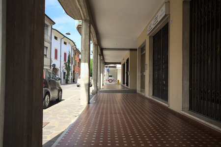 Modern porch under a building with shops closed by metallic shutters by the edge of a street on a sunny dayの写真素材