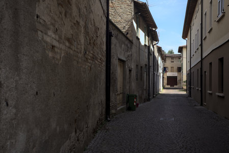 Alley in the shade with an abandoned shop at the end of it seen from an arch at the beginning of the street on a sunny day in an Italian townの写真素材
