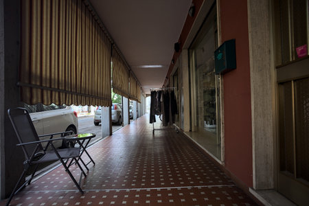 Porch in the shade with curtains in the gaps between columns and chairs and a clothes rack in the middle of it in an Italian townの写真素材