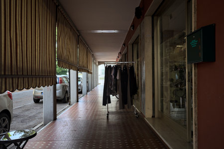 Porch in the shade with curtains in the gaps between columns and chairs and a clothes rack in the middle of it in an Italian townの写真素材