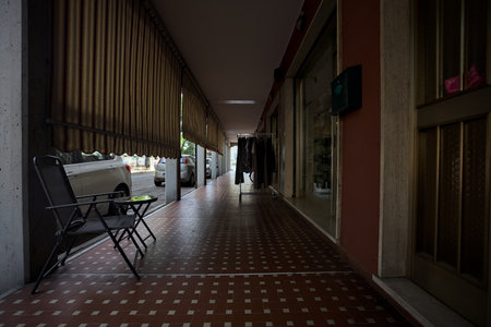 Porch in the shade with curtains in the gaps between columns and chairs and a clothes rack in the middle of it in an Italian townの写真素材