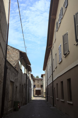 Alley in the shade with an abandoned shop at the end of it seen from an arch at the beginning of the street on a sunny day in an Italian townの写真素材