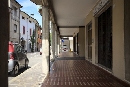 Modern porch under a building with shops closed by metallic shutters by the edge of a street on a sunny dayの写真素材