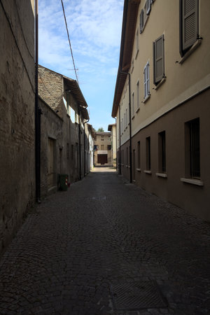 Alley in the shade with an abandoned shop at the end of it seen from an arch at the beginning of the street on a sunny day in an Italian townの写真素材