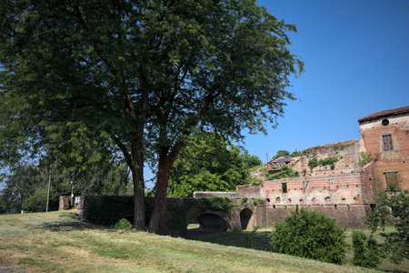 Square with a poplar by its edge and an abandoned palace in the background surrounded by trees on a sunny day in the Italian countrysideの写真素材