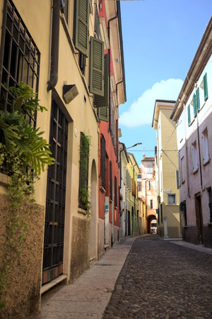 Cobbled street in the shade that leads to a covered passage under a building in an Italian town on a...