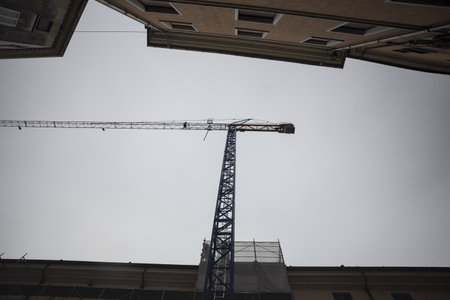 Crane towering over a street with a cloudy sky as background framed by buildings