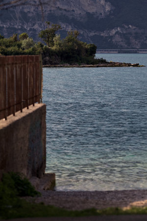 Boundary wall with a fence over it by the shore of a lake in the mountains on a partially cloudy dayの写真素材