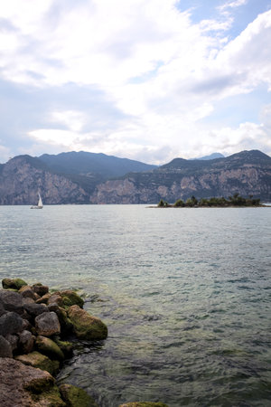 Small island on a mountain lake seen from the shore on a partially cloudy dayの写真素材