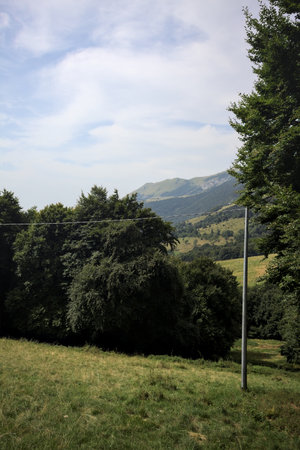 Meadows and groves dotting the slopes of a mountain with the mountain ridge in the distance seen...