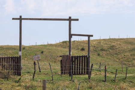 Wooden gate next to a trail that leads to a field in the mountain on a sunny dayの写真素材