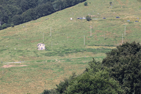 Abandoned gray house in a field by the edge of a winding road on the slope of a mountain seen from Afarの写真素材