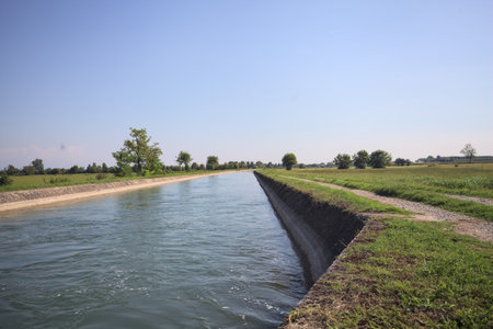 Flowing water in a diversionary channel bordered by trails in the middle of a meadow on a sunny day in the Italian countrysideの写真素材