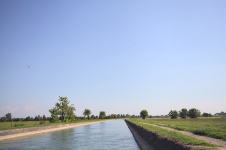Flowing water in a diversionary channel bordered by trails in the middle of a meadow on a sunny day in the Italian countrysideの写真素材