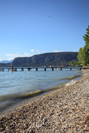 Pier stretching over a lake on a sunny day with people on it and a mountain ridge in the background