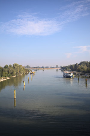 Diversionary channel with poles in it and a moored boat with the sky casted in the water and a tree framing the sceneの写真素材