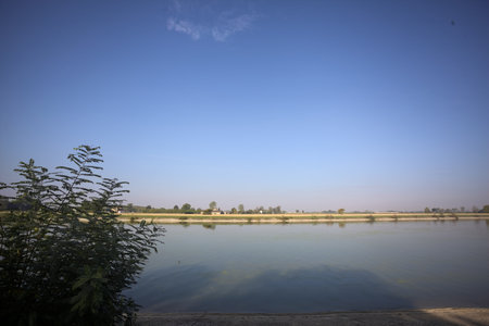 Plowed fields and country manors on them on the bank of a river on a sunny day seen from afar