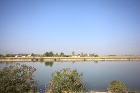 Plowed fields and country houses on them on the bank of a river on a sunny day in the Italian...