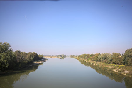 River bordered by trees on an embankment reflected in the water on a sunny day seen from aboveの写真素材