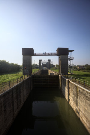 Sluices on a dam in a diversionary channel in the Italian countryside on a sunny day seen from above a bridgeの写真素材