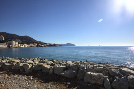Breakwater with rocks by the sea on a sunny day with a city and cliffs in the distanceの写真素材