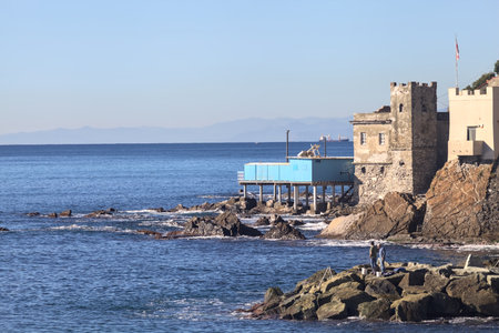 Blue stilt house on a cliff by the seashore on a sunny day with boats and ships sailing in the...