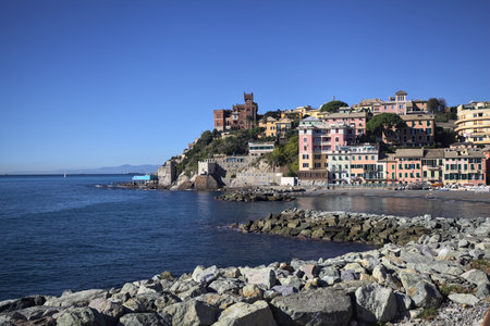 Breakwater with rocks by the sea on a sunny day with a city and cliffs in the distanceの写真素材