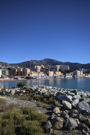 Breakwater with rocks by the sea on a sunny day with a city and cliffs in the distanceの写真素材