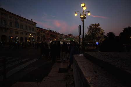 Verona, Italy - 8TH DECEMBER 2025 - Corner of a pavement with a street light and people passing by, at the entrance of the Christmas market in Bra squareのeditorial素材