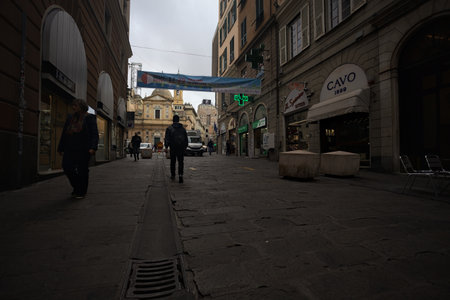 Genoa, Italy - 12TH NOVEMBER 2025 - San Lorenzo avenue in the Caruggi quarter with people walking by and opened shops and the Saints Ambrogio and Andrea church at the end of itのeditorial素材
