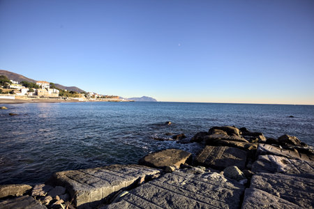 Tip of a promontory with buildings and a cliff away in the distance seen from a small cove and framed by rocks of a breakwaterの写真素材