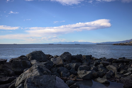 A concrete wall next to a sea with the sunlight cast on water, and boats sailing on it, counterlit by the sunの写真素材