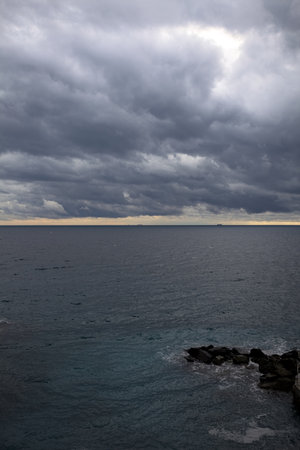 Sea stretching to the horizon on a cloudy day at twilight with rocks from a small cove seen from aboveの写真素材