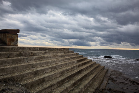 Staircase by the edge of a cliff alongside rocks on a cloudy day at twilightの写真素材