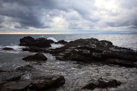 Small staircase on a rock next to a cliff in a cove by the sea on a cloudy day at twilight