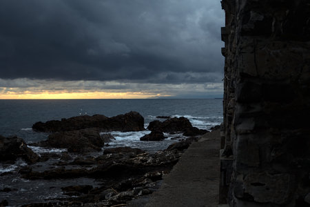 Arches of a viaduct by the edge of the sea, on the rocks of a breakwater, seen on a cloudy day at...