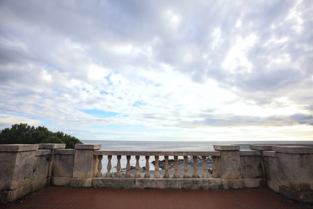 Railing on the balcony in a promenade, framing the sea, with a cloudy sky above, on a winter dayの写真素材