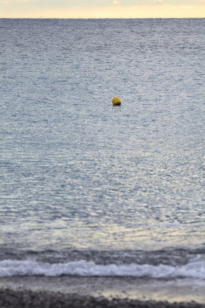 Yellow buoy on the sea, seen from the beach, at sunset