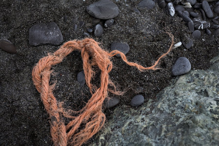 Orange rope on the sand next to a rock, seen from above and up closeの写真素材