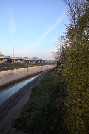 Diversionary channel with a viaduct on one edge and a park on the other, framed by a tree with falling leaves, at sunsetの写真素材