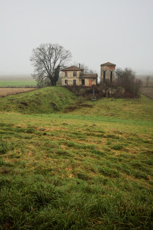 Abandoned dam building in a field, framing a ditch with water, with a bare tree next to it, on a...